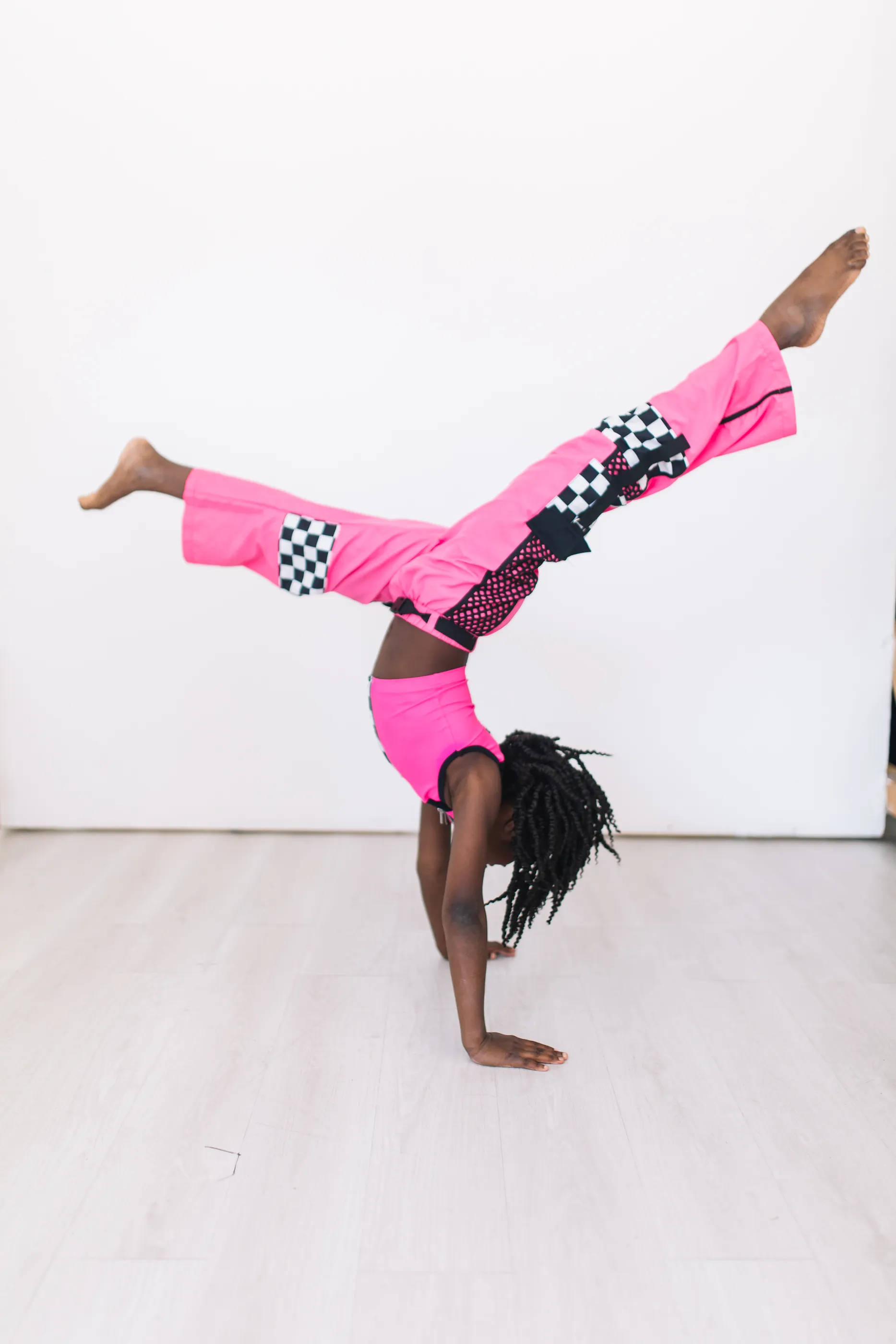 A girl in a hot pink dance outfit mid-handstand, legs in the air.