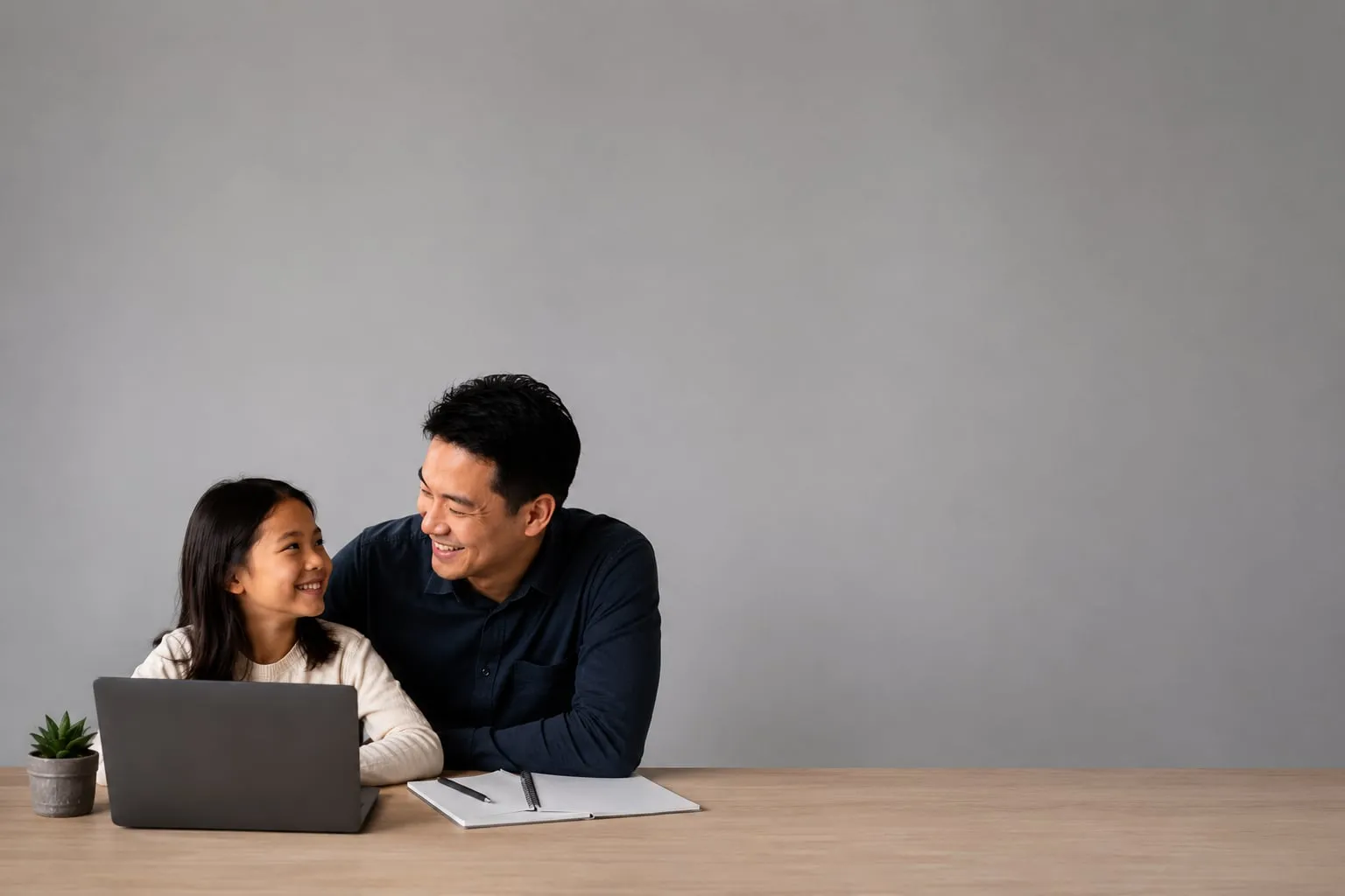 A parent at a kitchen table with a laptop, reading.